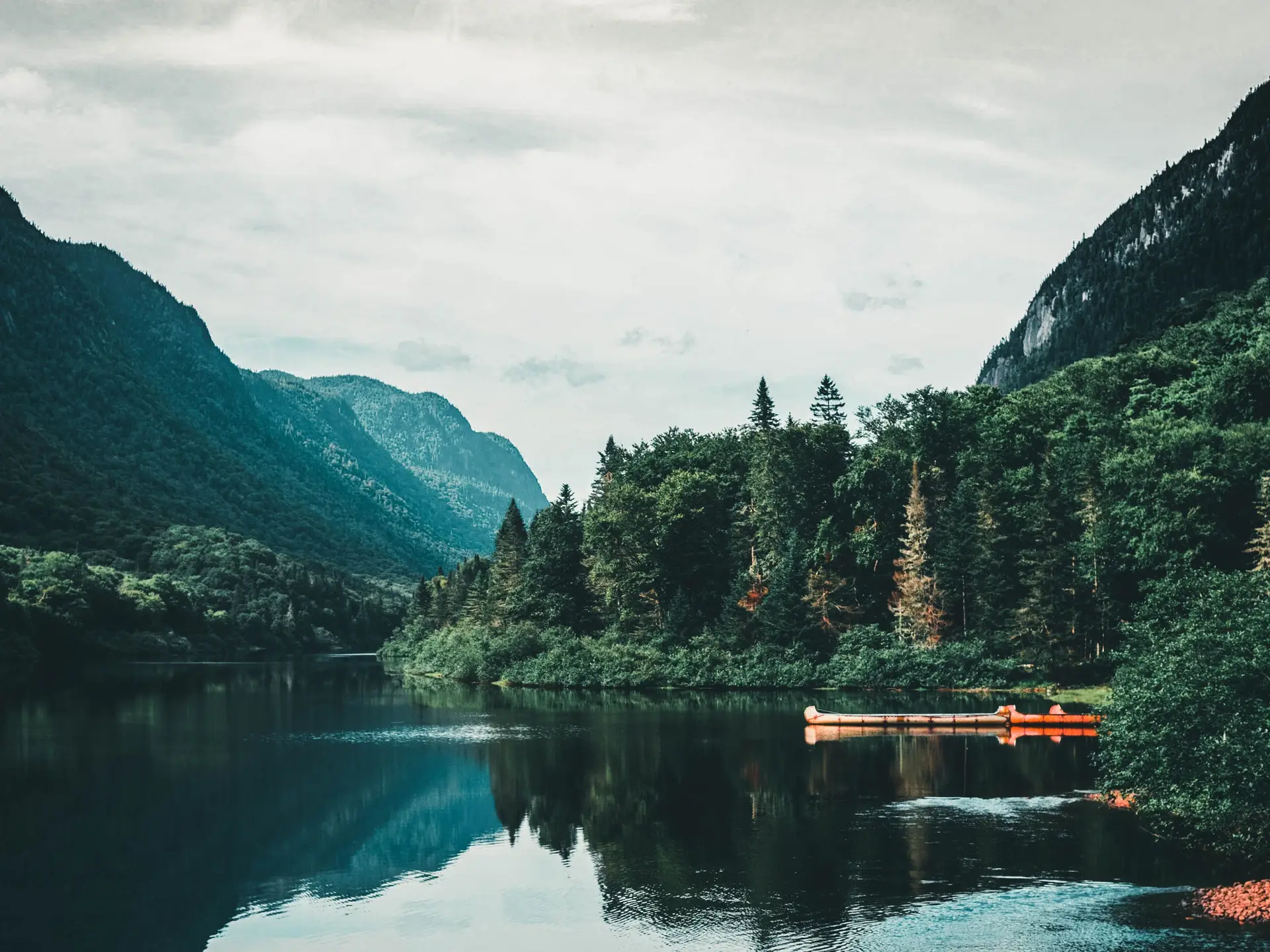 Tranquil alpine lake surrounded by emerald coniferous forest and quiet Canadian mountains