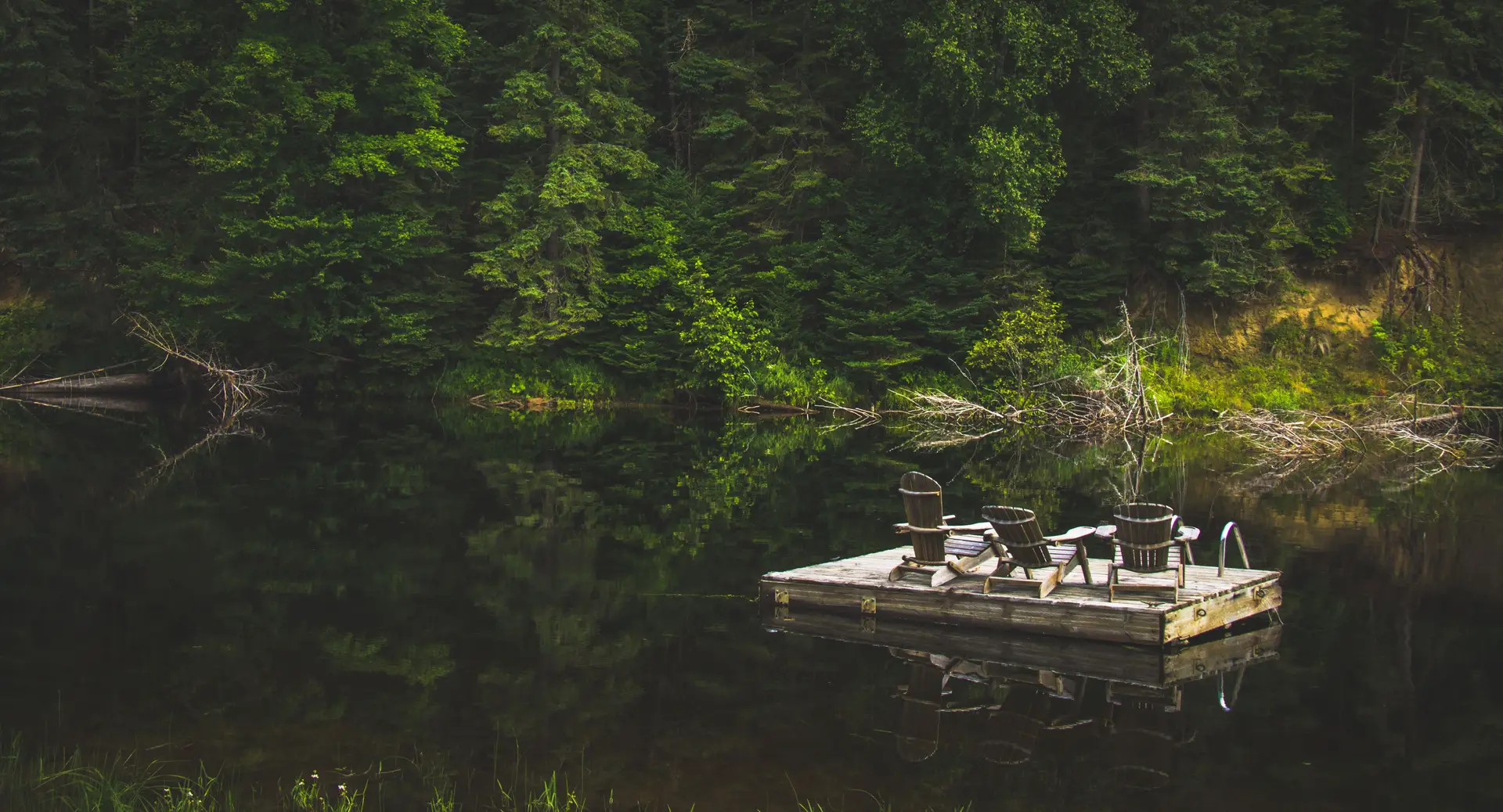Lakeside wooden dock with solitary chairs overlooking serene reflective water and pine trees