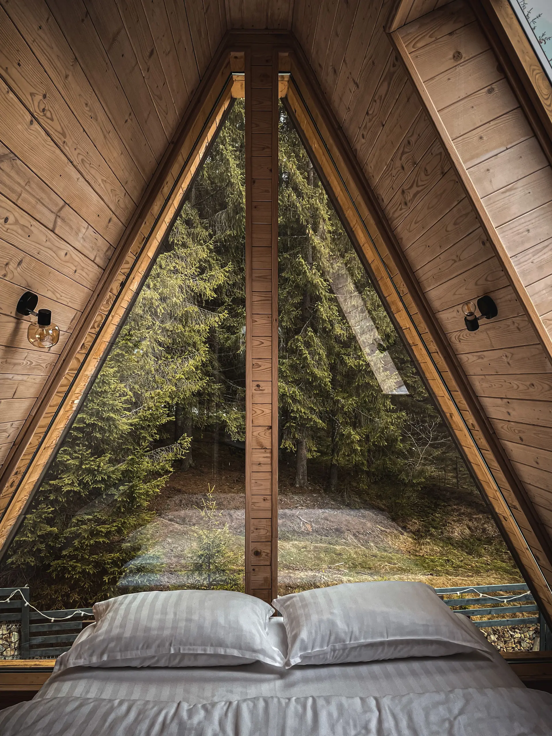 Serene A-frame cabin bedroom with high triangular windows facing towering fir trees